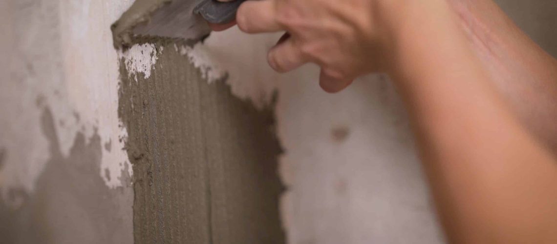 Aligning the adhesive on the wall for gluing the tiles. The builder attaches the tiles to the wall with cement. A male tiler manually glues ceramic tiles to the bathroom wall.