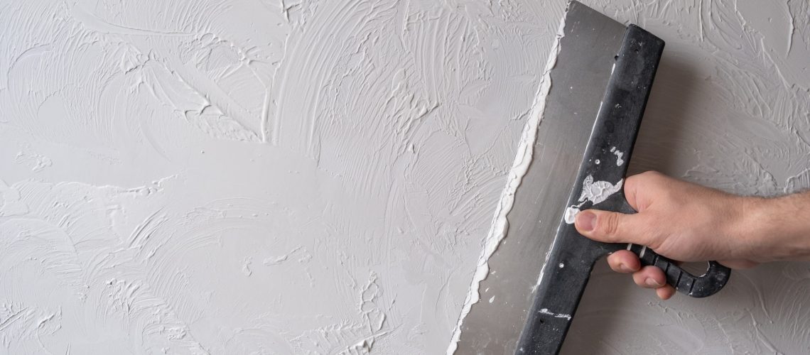 Applying decorative putty. White abstract texture of surface covered with putty. textured background of filler paste applied with putty knife in irregular dashes and strokes. Rough surface plaster